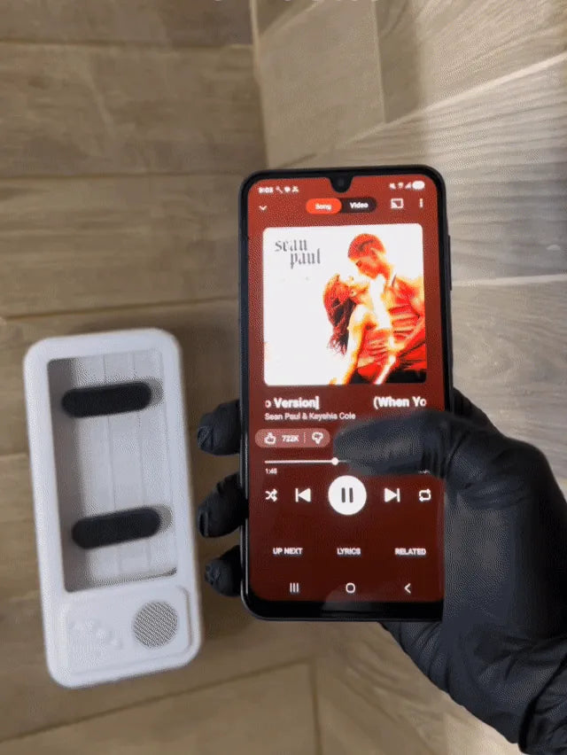 Original product demonstration with music playing on a phone beside a white shower dock